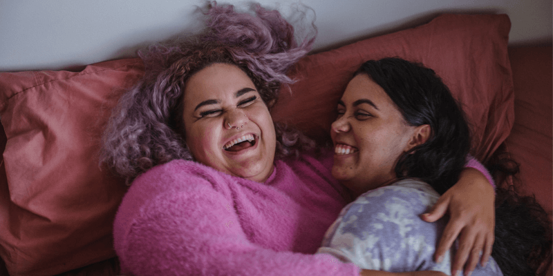 Two women hug and laugh together on a bed