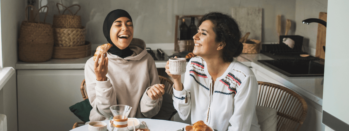 Two female friends having breakfast in their kitchen and laughing together