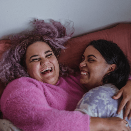 Two women laughing and hugging eachother on a bed